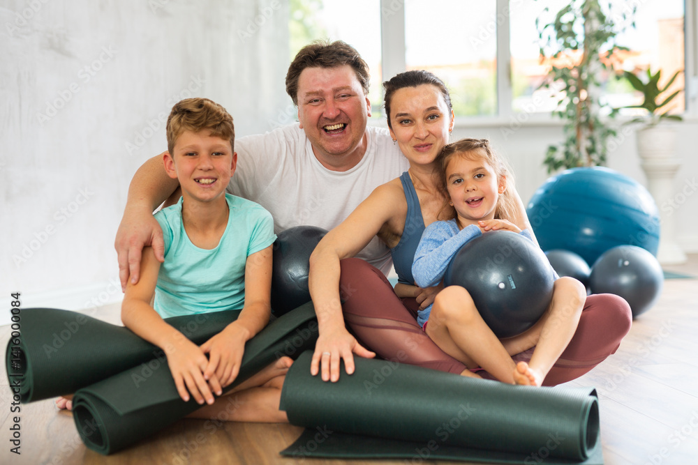 Obraz premium Family with two kids posing with yoga mats and softballs in fitness studio