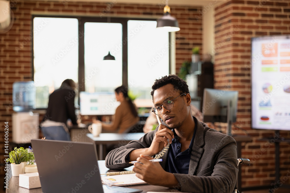 African American employee with pen in hand, providing insights to a client on a call, discussing business growth. Black man in wheelchair using a landline phone while reviewing company research data. African American employee with pen in hand, providing insights to a client on a call, discussing business growth. Black man in wheelchair using a landline phone while reviewing company research data.