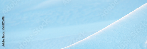 Wide panoramic winter background with snowy ground. Natural snow texture. Wind sculpted patterns on snow surface. Closeup top view with copy space.