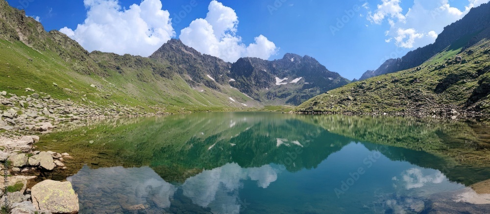 Fototapeta premium A serene mountain lake reflects clouds and surrounding peaks beautifully