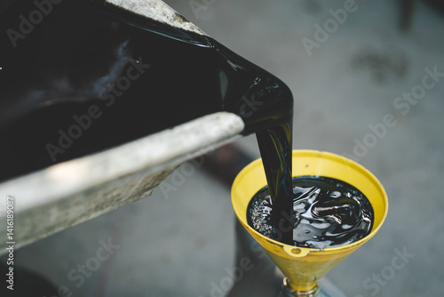 Obraz na płótnie Old engine oil. Pouring old black oil of car engine from oil pan into bottle on top view lubrication used for recycle. w salonie