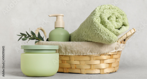 Wicker basket with clean towel, cosmetic products and eucalyptus branch on light background