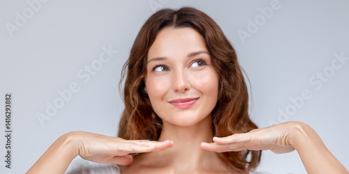 Trendy studio beauty shot of a young woman with radiant skin, softly framing her face with both hands. Ideal for cosmetic ads, skincare branding, and cheerful beauty-focused marketing.
