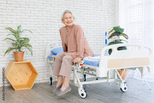 Obraz na płótnie Asian senior woman smiling, happy old patient with grey hair in brown dress thumb up while sitting on bed in hospital, Healthcare elderly rehabilitation supporting care therapy center wellness being. w salonie