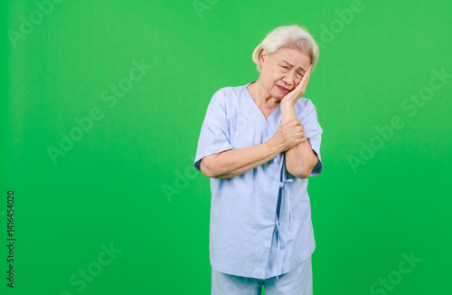 Obraz na płótnie Portrait of asian senior woman wearing patient's set, retired older lady having backache pain wrist, arm and body standing over isolated green background, Elderly people healthcare facility concept. w salonie