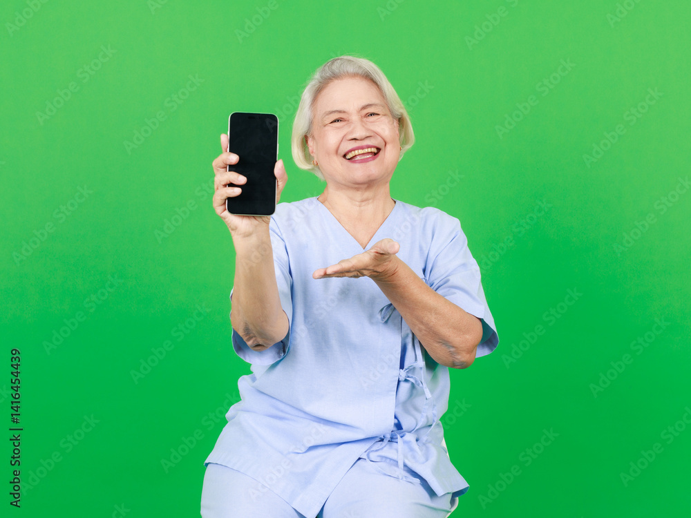 Portrait of asian senior woman wearing patient's set, retired older lady holding show smartphone screen smile sitting over isolated green background, Elderly people healthcare insurance health care.