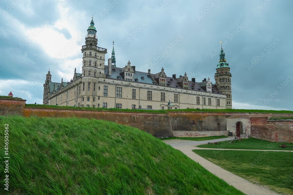 Fototapeta premium Kronborg Castle, the historic setting for Shakespeare's Hamlet, stands majestically behind green grassy ramparts and weathered brick fortifications, its Renaissance towers in Helsingor, Denmark