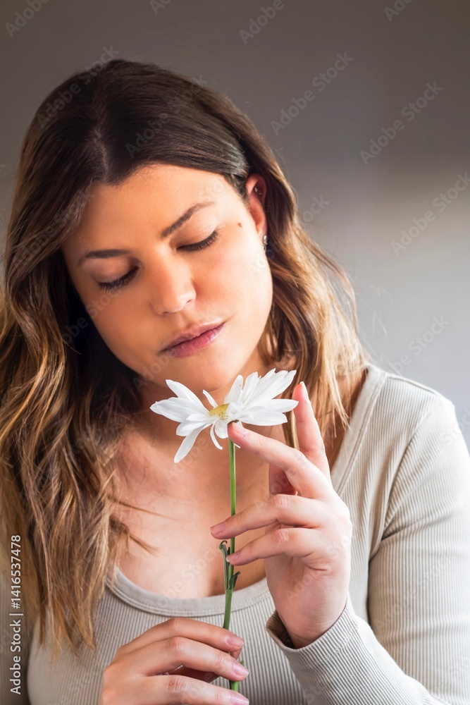 Serene young woman holding a white daisy with closed eyes Serene young woman holding a white daisy with closed eyes
