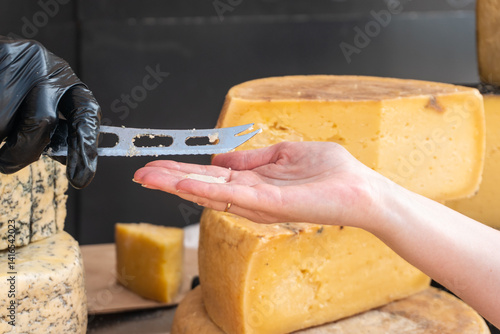 A vendor slices a piece of cheese with a knife at a farmers market