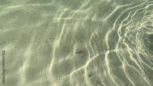 Repeat ripple wave of sea with sunny reflection over sand beach under clear water background.