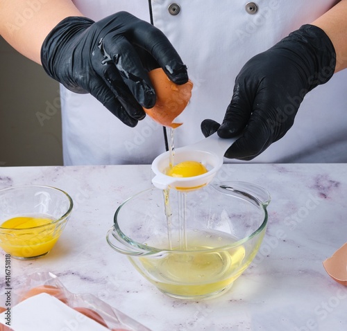 Woman in black gloves separating egg whites from yolks to make dough, dessert or meringue. Chef at work in the kitchen.
