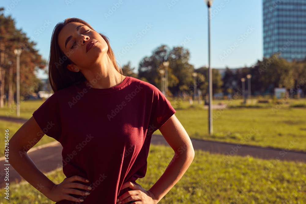 Young woman warming up for exercise and jogging in urban park during sunny summertime day.