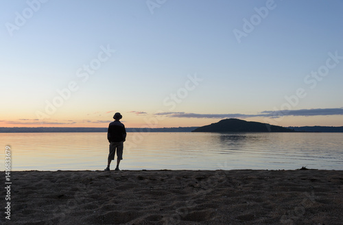 Obraz na płótnie Man standing along on the beach at sunset. Mokoia Island in the distance. Lake Rotorua. w salonie