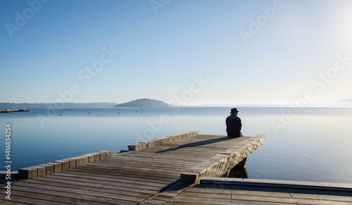 Obraz na płótnie Man sitting on the boardwalk at lakefront of Lake Rotorua. Mokoia Island in the distance. Rotorua. w salonie