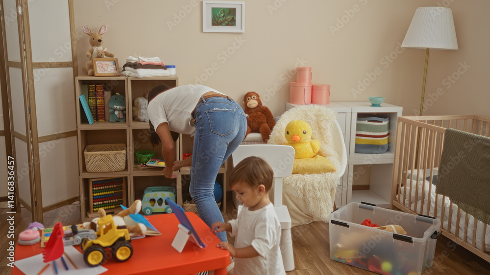 Woman organizing nursery with son playing nearby in home setting filled with toys and a crib, showcasing a cozy family environment.