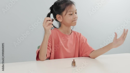 Elementary school kid girl is sitting and painting her nails by herself, with different poses, expressions of both liking and disliking her work. Concept of a girl who loves beauty, white background.