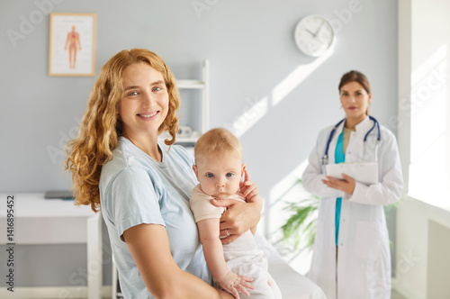Obraz na płótnie Portrait of young cheerful mother with toddler baby visiting female pediatrician in medical office. Happy mom holding newborn kid on her hands during medical checkup in clinic. Childcare concept. w salonie