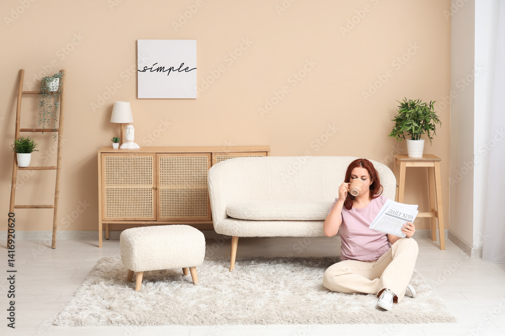 Young woman with newspaper drinking tea on carpet at home