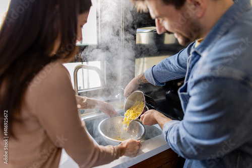 Chef and sous chef draining steaming hot pasta in a colander, working together in a cozy kitchen sink, preparing a delicious meal
