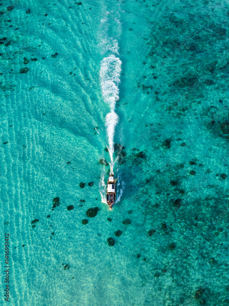 A fast boat glides through shallow crystal-clear waters, leaving a white trail on the turquoise sea in Thailand.