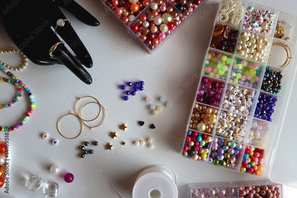 Hand figurine, colorful friendship bracelets, necklaces, various beads and DIY supplies on the table. Making jewelry at home. Flat lay.