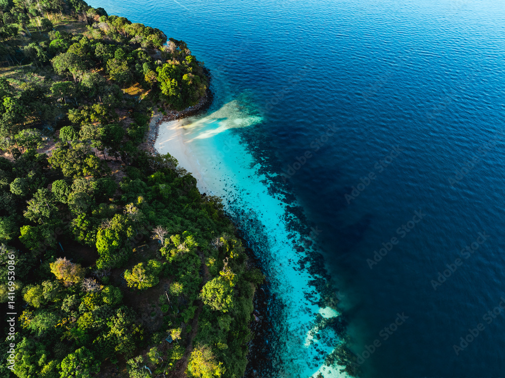 Tropical forest meets a white sandy beach with turquoise water along a curved island coastline, seen from above in Thailand.