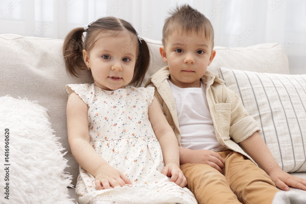 Portrait of cute little twins sitting on sofa at home Portrait of cute little twins sitting on sofa at home