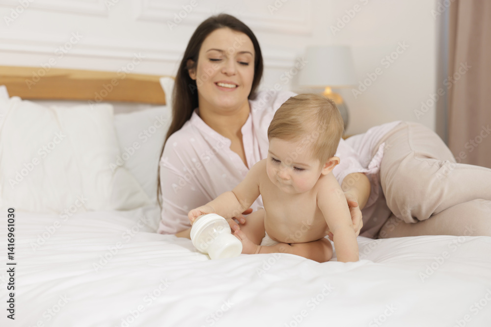 Mother with her little baby and feeding bottle of milk on bed at home Mother with her little baby and feeding bottle of milk on bed at home