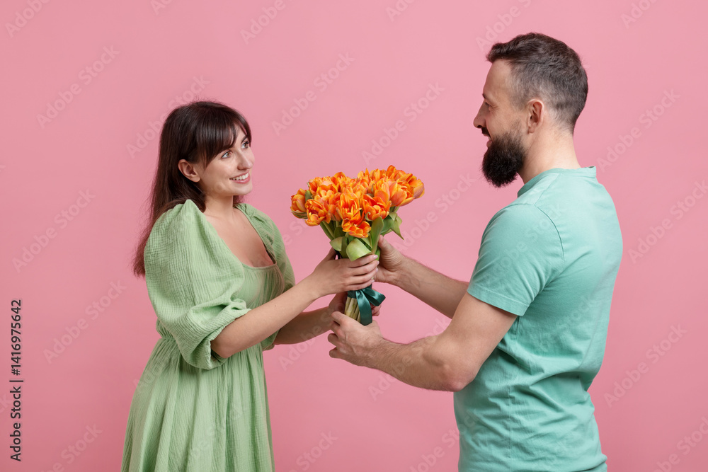 Man presenting bouquet of beautiful tulips to his beloved woman on pink background Man presenting bouquet of beautiful tulips to his beloved woman on pink background