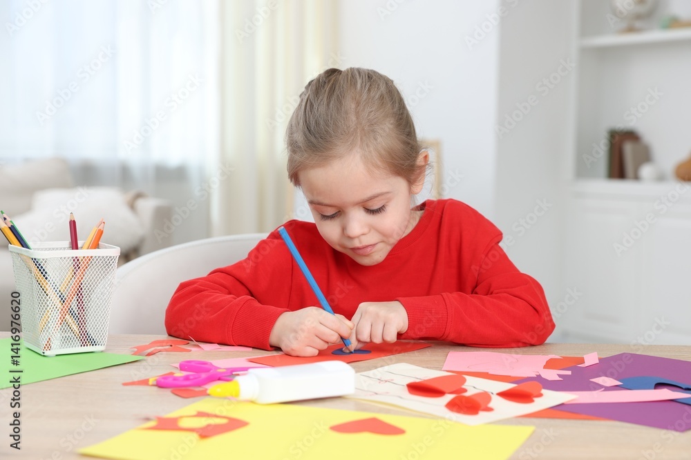 Little girl making handmade project with color paper and pencil at table indoors Little girl making handmade project with color paper and pencil at table indoors