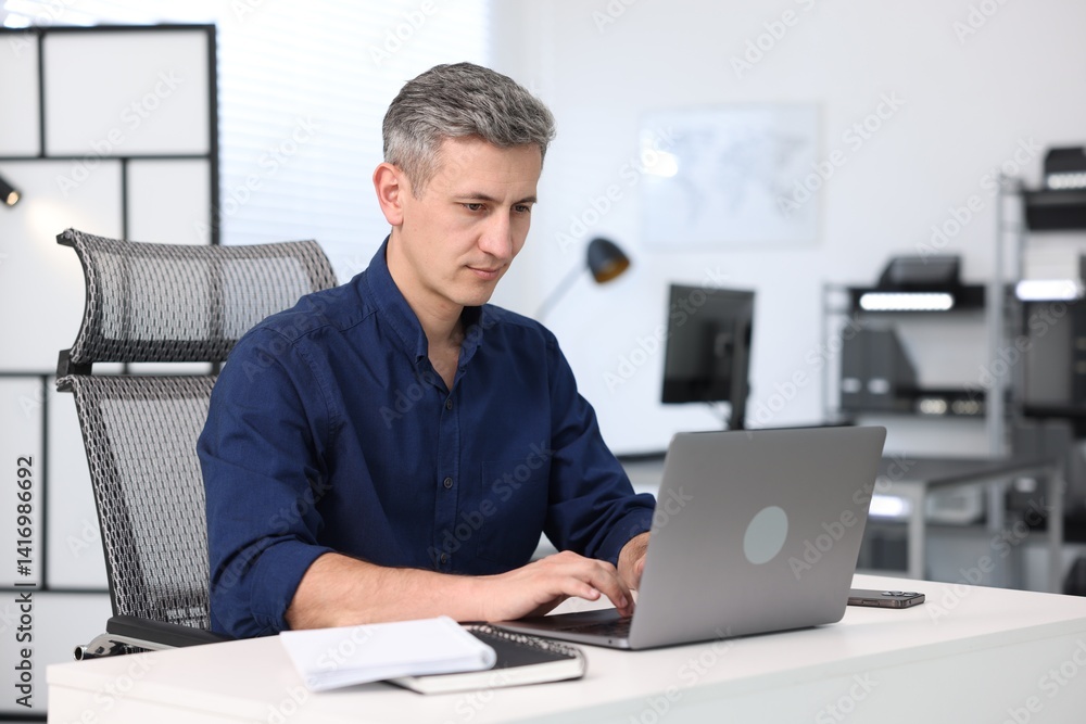 Businessman working on laptop at table in office Businessman working on laptop at table in office