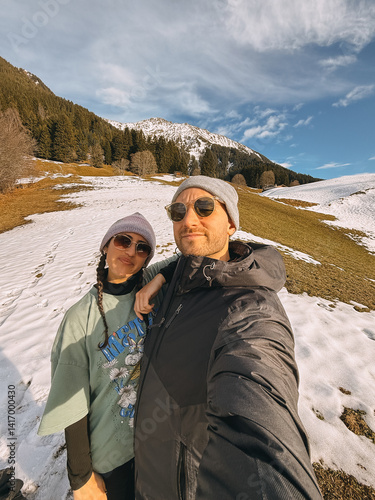 Tourists enjoying winter holidays in a snowy mountain landscape, capturing a selfie against a backdrop of snow-capped peaks and alpine scenery