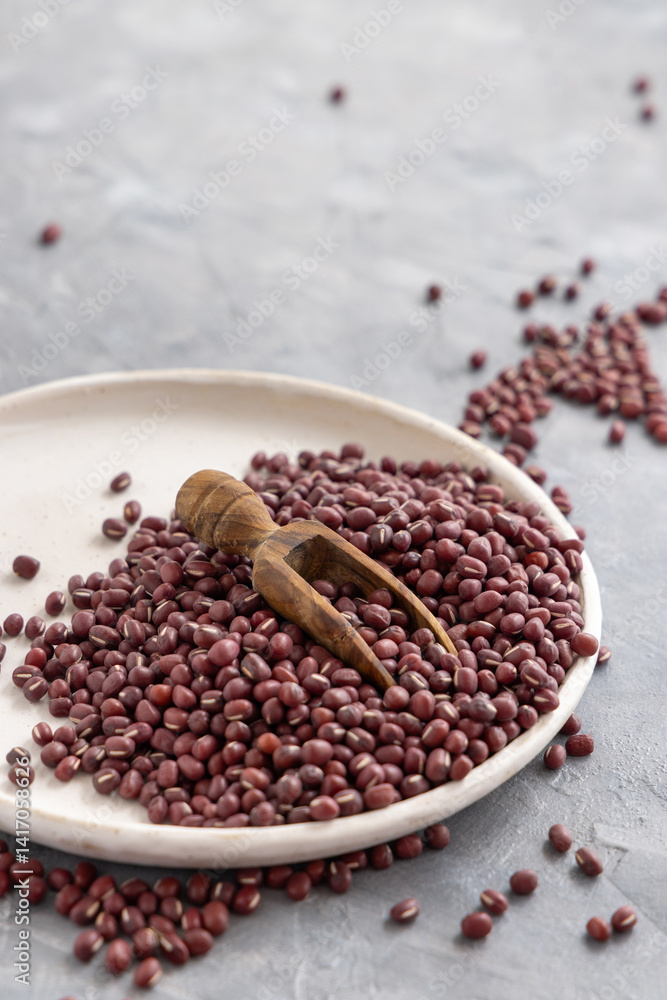 Plate full of dried red azuki beans with a wooden scoop closeup. East Asian legumes, vegetarian food Plate full of dried red azuki beans with a wooden scoop closeup. East Asian legumes, vegetarian food