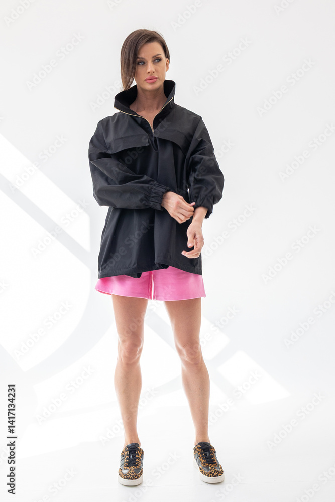 Elegant woman in black windbreaker jacket and pink shorts on light background. Fashionable female style. Studio photography. Vertical photo Elegant woman in black windbreaker jacket and pink shorts on light background. Fashionable female style. Studio photography. Vertical photo