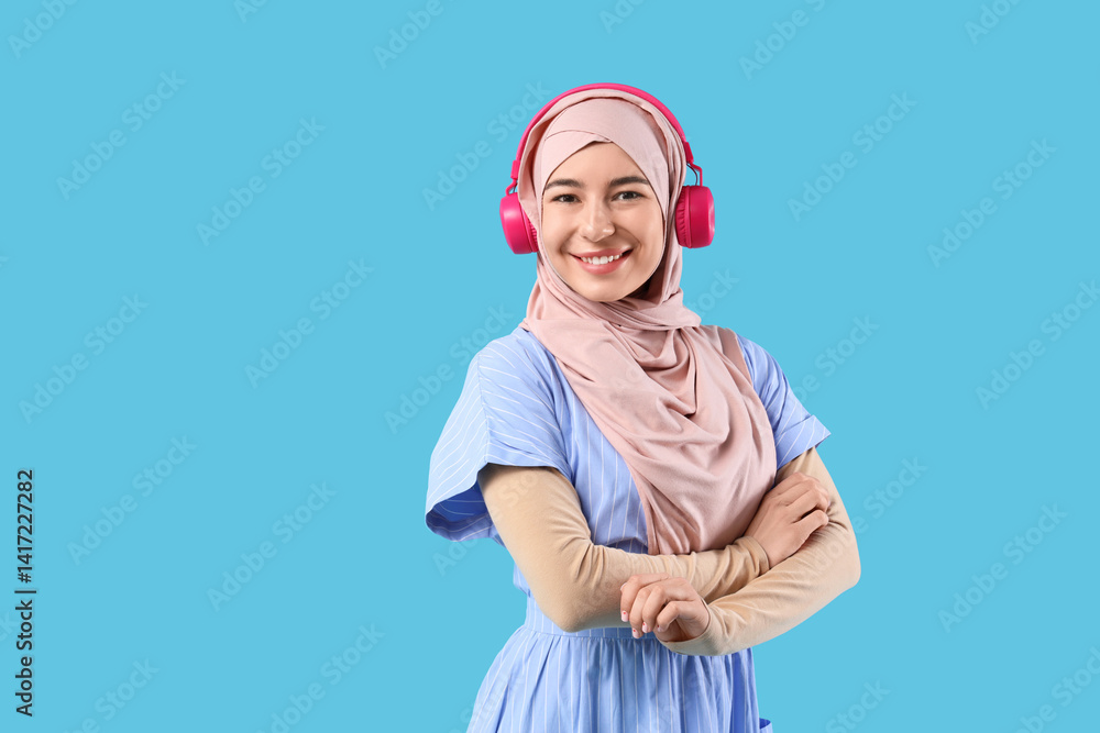 Beautiful young Muslim woman in hijab and modern headphones on blue background Beautiful young Muslim woman in hijab and modern headphones on blue background