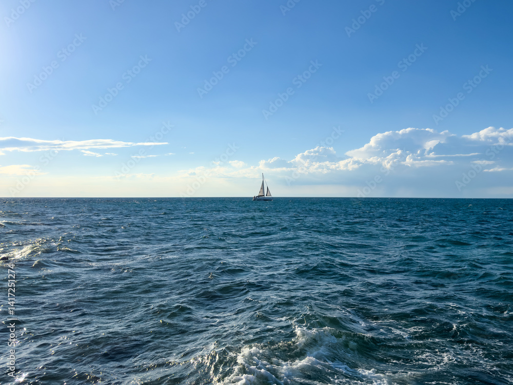 Obraz premium sailboat on the in deep blue open sea with calm waves on bright sky background with copy space. sea surface