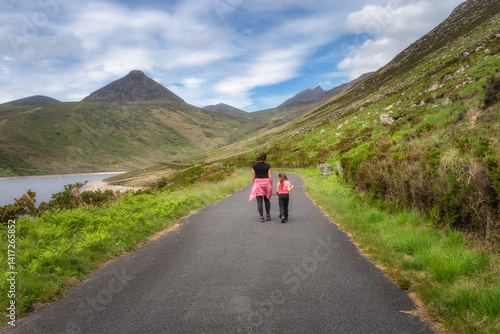 A joyful mother and her excited child stroll along a scenic pathway, surrounded by vibrant greenery and stunning Mourne Mountains, creating unforgettable memories, Northern Ireland