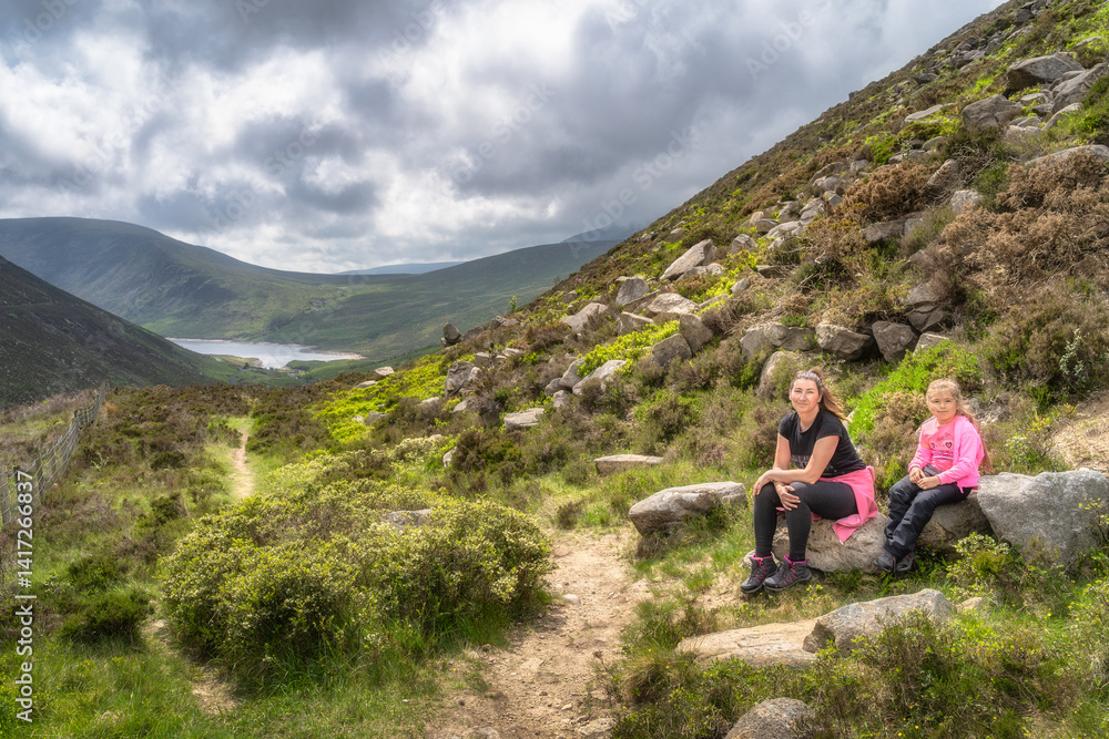 A family delights in a peaceful and memorable hike amidst breathtaking Mourne Mountains scenery that showcases lush greenery and a serene, sparkling Silent Valley Reservoir view, Northern Ireland