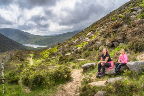Obraz na płótnie A family delights in a peaceful and memorable hike amidst breathtaking Mourne Mountains scenery that showcases lush greenery and a serene, sparkling Silent Valley Reservoir view, Northern Ireland w salonie