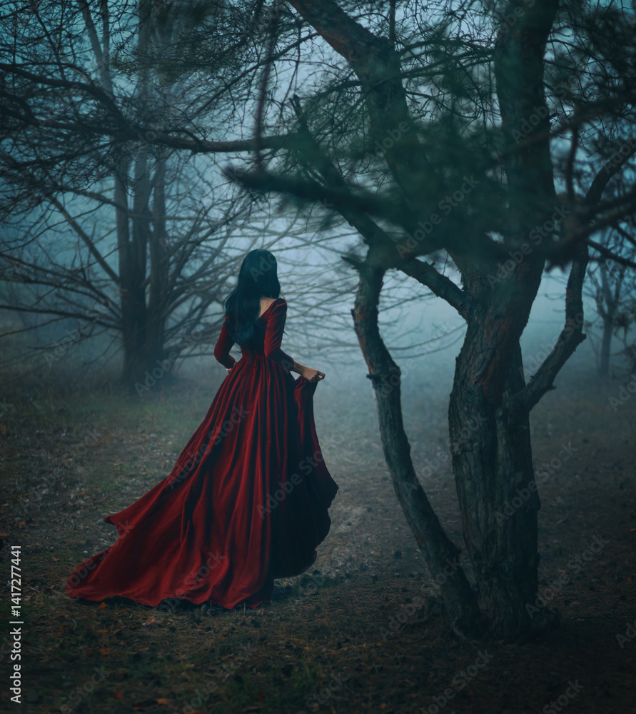 Fototapeta premium Art photo real person Gothic girl walking running in dark foggy forest trees, velvet red long medieval old style long dress train fly wind. Fantasy Woman Black hair back rear view fairy princess