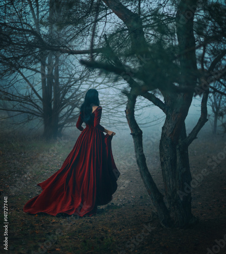 Art photo real person Gothic girl walking running in dark foggy forest trees, velvet red long medieval old style long dress train fly wind. Fantasy Woman Black hair back rear view fairy princess