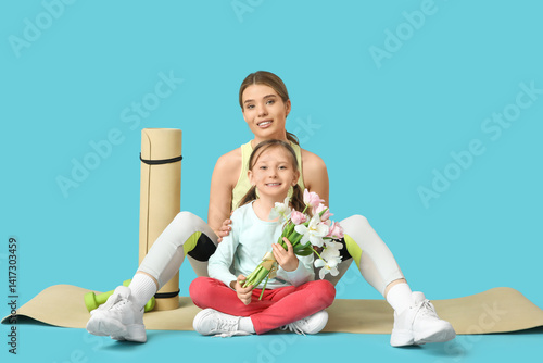 Obraz na płótnie Sporty young mother and her cute little daughter with bouquet of flowers sitting on blue background. Mother Day celebration w salonie