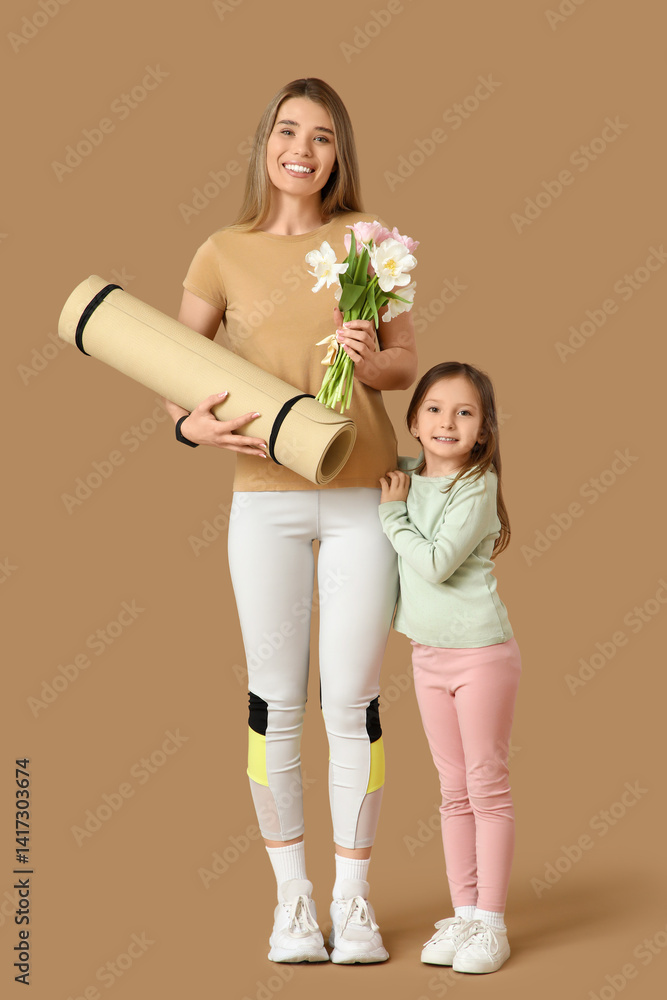 Sporty young mother with bouquet of flowers and her cute little daughter exercising on beige background. Mother Day celebration