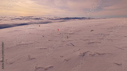Gorgeous aerial drone footage view of people flying kites and surfing with them in Norway Varanger Arctic Kite Enduro competition during a beautiful sunny winter day. The kite surfing creates shadows.