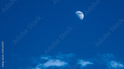 A waxing gibbous moon shines in a deep blue sky with wispy white clouds at the bottom. Tranquil night or twilight scene.