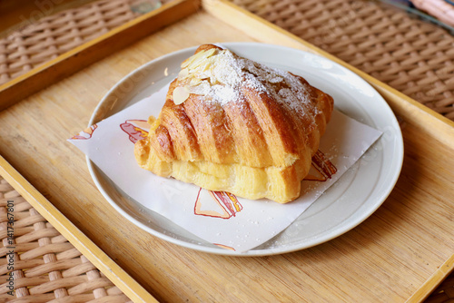 Top view single croissant topped with almonds placed on a wooden tray,homemade dessert bakery