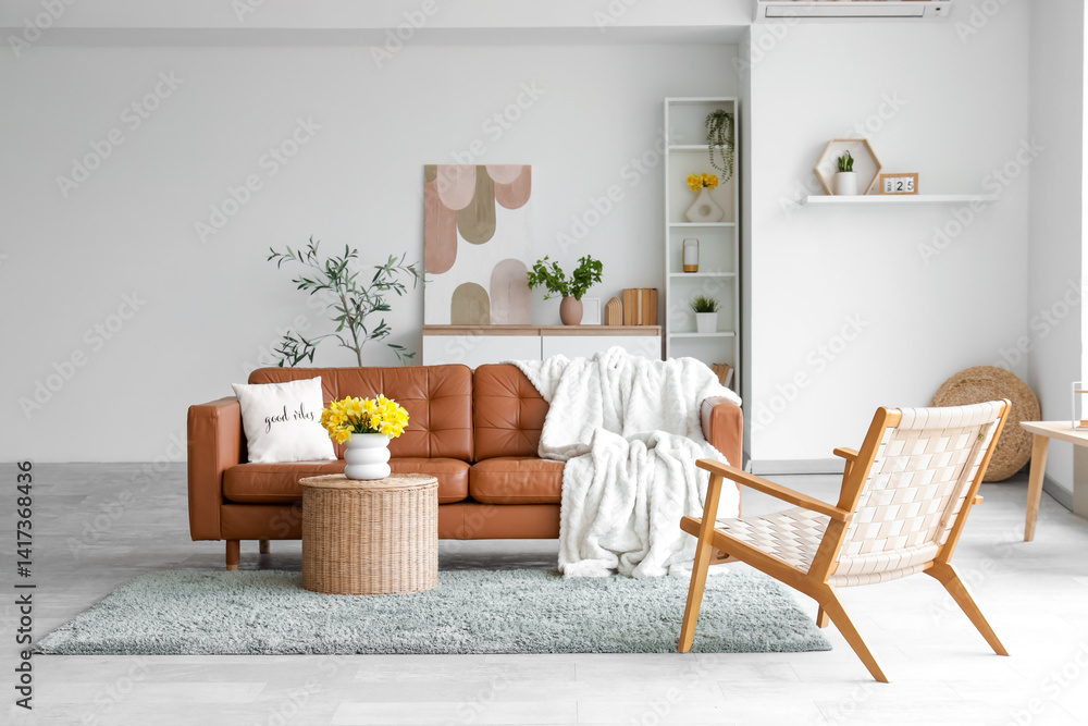 Interior of light living room with brown sofa, armchair and daffodils in vases