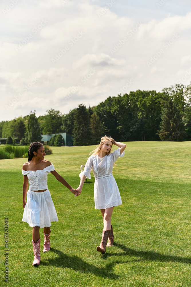 Naklejka premium Young couple walks hand in hand through a sunlit green meadow enjoying their love filled day