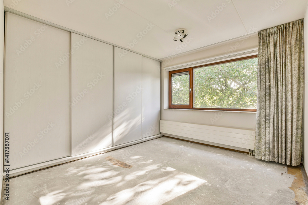 Obraz premium A modern, unfurnished room showcasing large windows that invite natural light, featuring minimalistic design and soft shadows on the floor.
