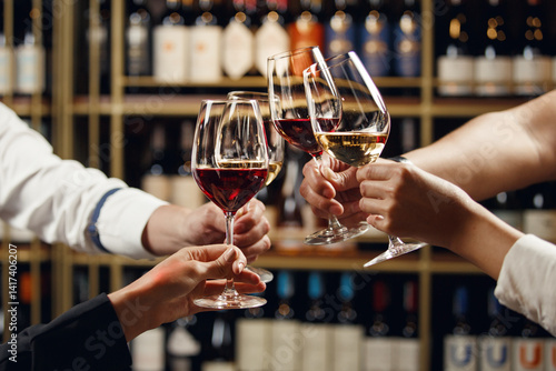 Big company people clinking glasses with red, rose and white wine on blurred cellar background. Men and women cheers with alcohol drink, closeup